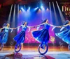 Four performers in blue costumes ride unicycles and hold hands on stage under bright lights part of the Drawn to Life Cirque du Soleil and Disney show