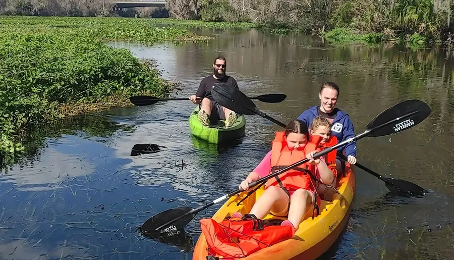 A family is kayaking on a calm river surrounded by greenery.