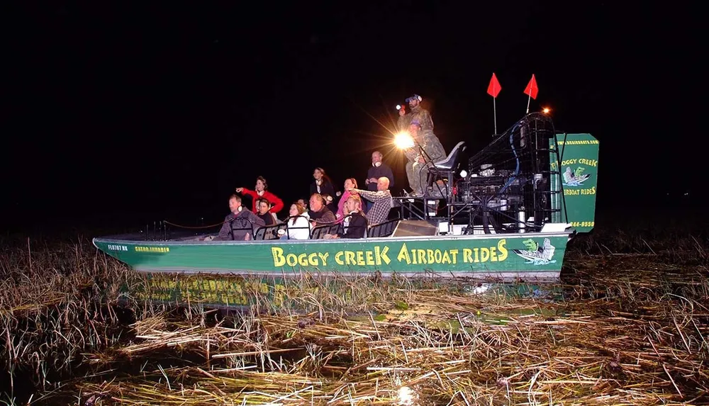 A group of people enjoy a nighttime airboat tour in a marshy area