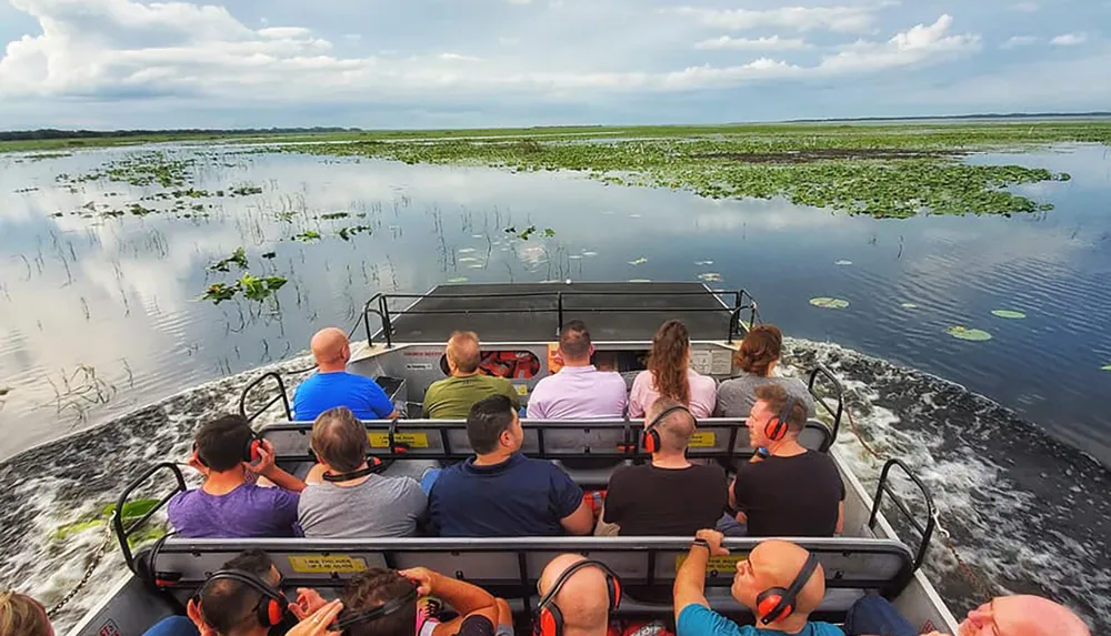 A group of people are enjoying an airboat tour through a scenic wetland area surrounded by vegetation and open skies