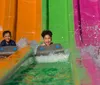 A person is smiling and enjoying a ride on a yellow inner tube down a vibrant blue water slide
