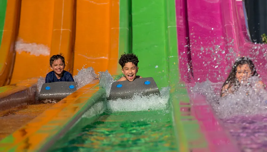 Three children are having a great time sliding down colorful water slides on a sunny day.