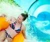 A person is smiling and enjoying a ride on a yellow inner tube down a vibrant blue water slide
