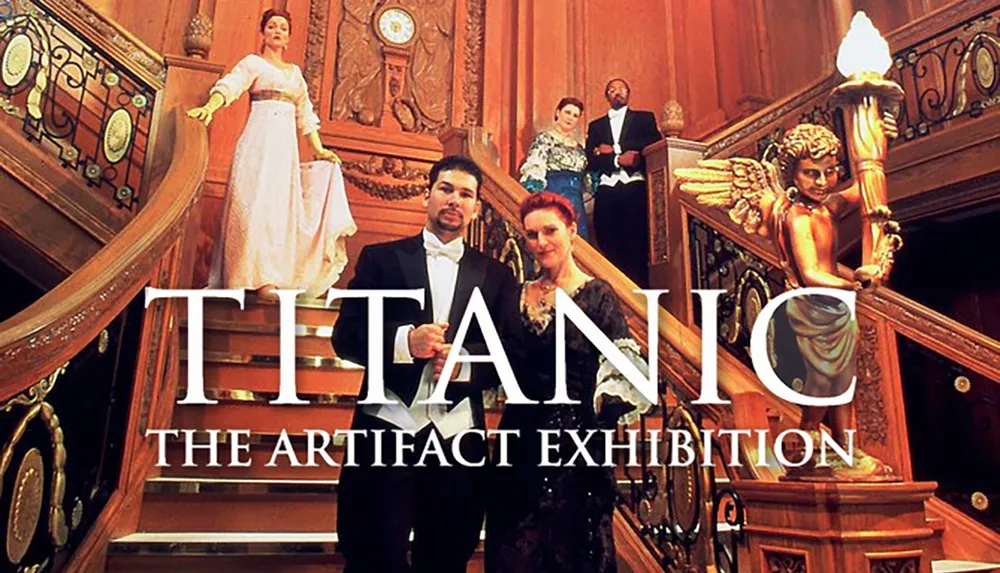 The image is a promotional photo featuring actors dressed in early 20th-century formal wear posing on a grand staircase replica for the TITANIC The Artifact Exhibition