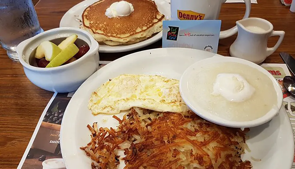 The image shows a traditional American breakfast with eggs hash browns pancakes grits fruit and beverages on a diner table