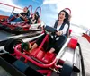 Three people are enjoying a thrilling ride on a go-kart track under a clear blue sky