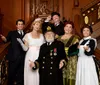 A group of people dressed in early 20th century attire representing characters from the Titanic era pose cheerfully on an ornate wooden staircase