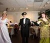 A group of people dressed in early 20th century attire representing characters from the Titanic era pose cheerfully on an ornate wooden staircase