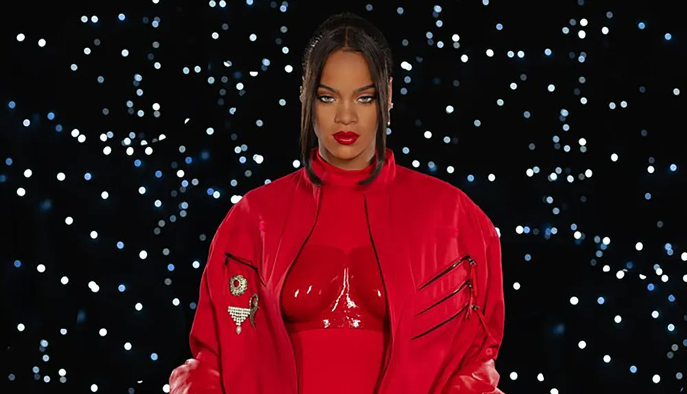 The image shows a person with a confident expression wearing a glossy red outfit with a high collar and decorative pin set against a bokeh light background