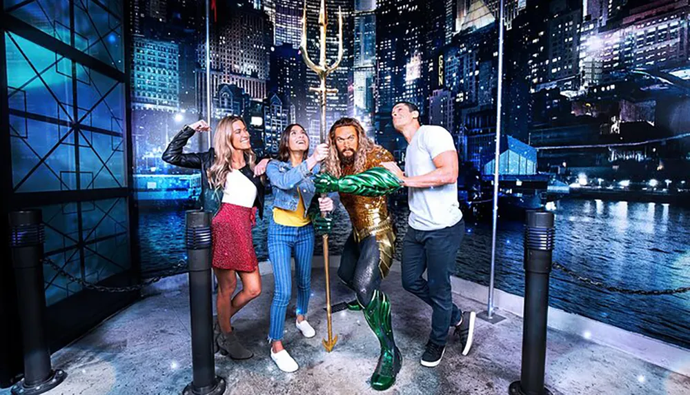 Three visitors are posing playfully with a wax figure of Aquaman at a themed exhibit simulating a superhero encounter against a vibrant cityscape backdrop