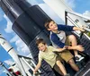 Two children are smiling and posing for a photograph with space rockets in the background likely at a space-themed park or museum