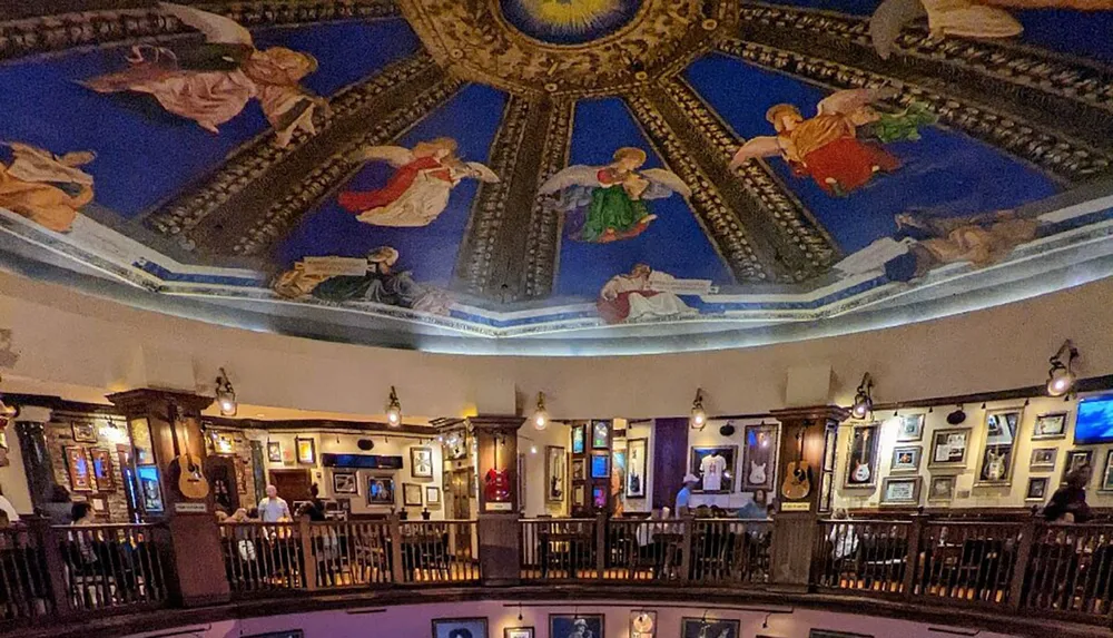 The image shows the interior of a pub with a vibrant ornately painted ceiling featuring what appears to be angelic figures surrounded by walls adorned with framed pictures and guitars