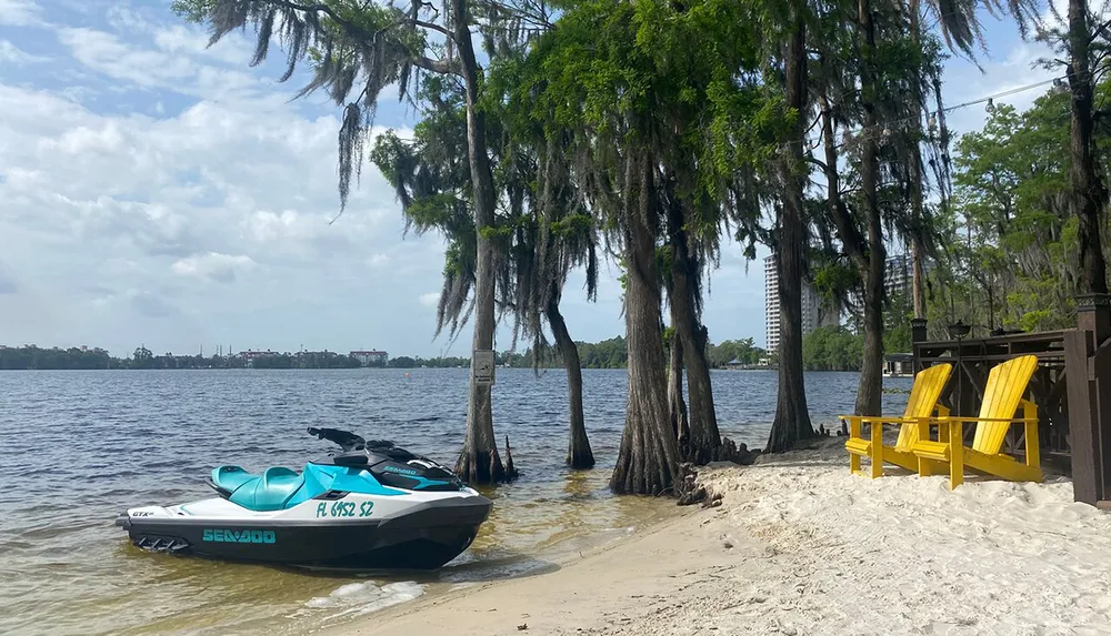 A personal watercraft is moored on the sandy shore of a lake with Spanish moss-draped trees next to a pair of inviting yellow Adirondack chairs