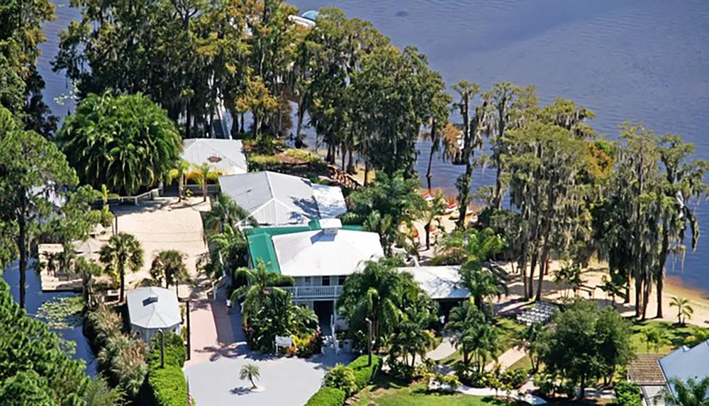 An aerial view of a tropical resort with multiple buildings surrounded by lush greenery and situated by a large body of water