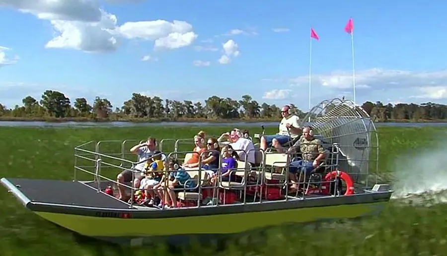 An airboat filled with passengers glides across what appears to be a marsh or wetland area, with the pilot standing at the rear.