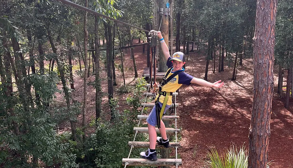 A child equipped with a harness and helmet is balancing on a rope course among the trees