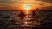 Two people are kayaking on the water during a beautiful sunset.