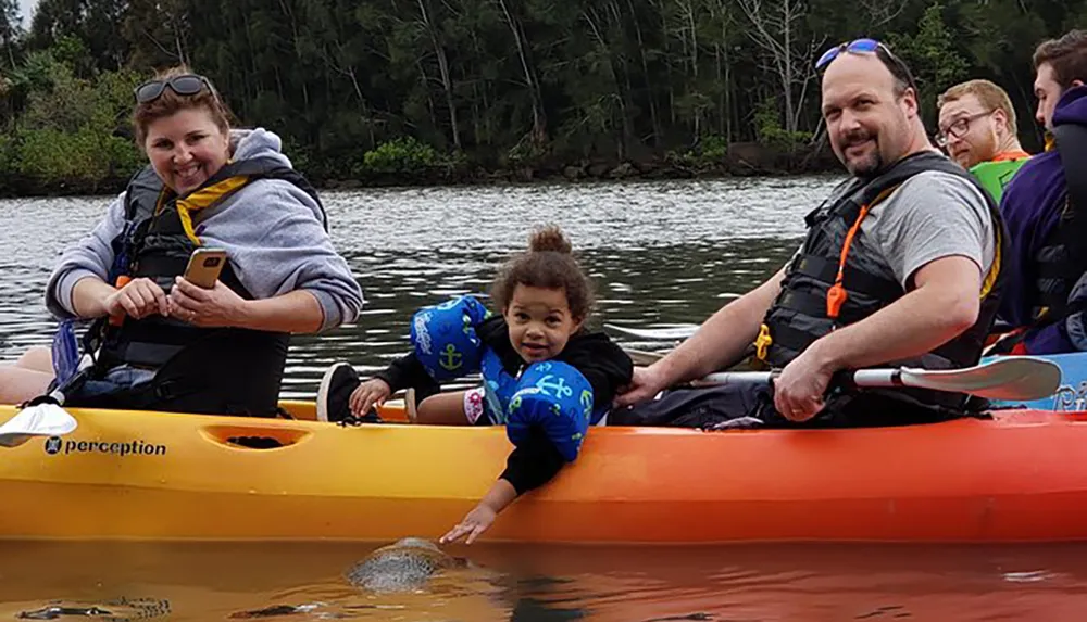 A group of people including a child wearing a life jacket is enjoying a kayaking adventure together on a river
