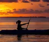 A person kayaks in tranquil waters against the backdrop of a vibrant sunset