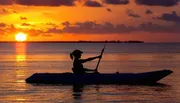 A person kayaks in tranquil waters against the backdrop of a vibrant sunset.