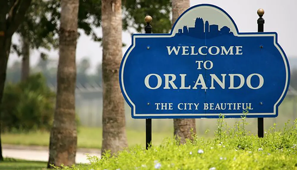 The image shows a blue welcome sign with white text reading Welcome to Orlando THE CITY BEAUTIFUL surrounded by greenery and palm trees