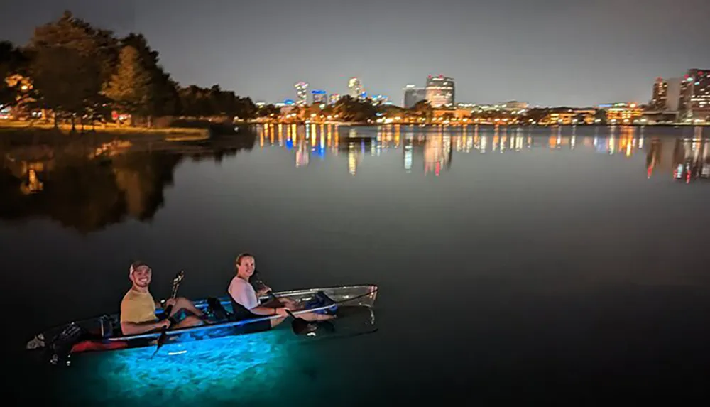 Two people are enjoying a nighttime kayak ride on a calm water body with a brightly illuminated city skyline in the background