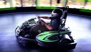 A person wearing a helmet is driving a go-kart on an indoor track, conveying a sense of speed and motion.