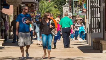 People stroll through a lively street lined with shops and restaurants on a sunny day.