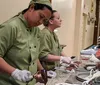 Two people in chef uniforms are working diligently in a kitchen one spreading chocolate on a dessert