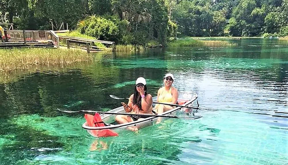 Two people are enjoying a sunny day on a clear turquoise river in a transparent canoe