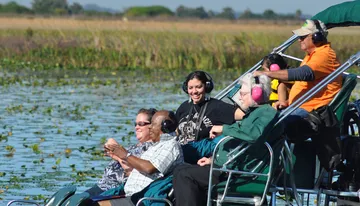 A group of people wearing headphones is enjoying a ride on a boat in a scenic wetland area.