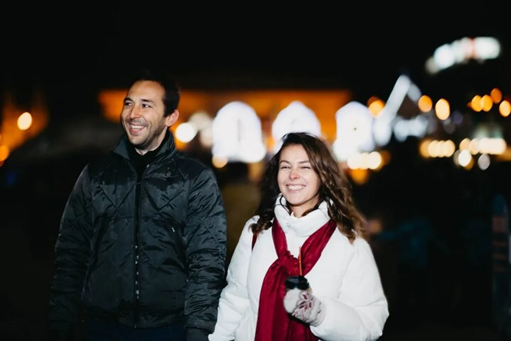 A man and a woman are smiling and enjoying a moment together outdoors at night with blurred lights in the background