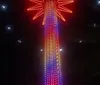 People are enjoying a nighttime swing ride against the backdrop of a brightly lit Ferris wheel and city lights