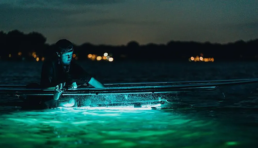 A person is kayaking at night using a see-through kayak illuminated from below highlighting the waters ethereal glow