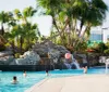 This image shows a sunny inviting resort pool area with lounge chairs and a water slide in the background ready for guests to enjoy a relaxing day
