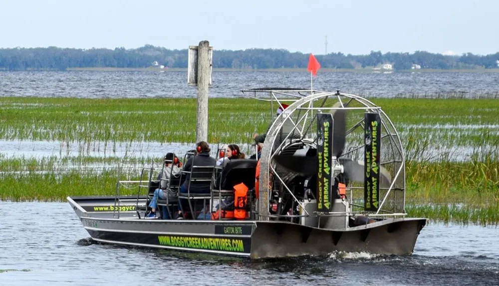 An airboat with passengers cruises through a grassy wetland area