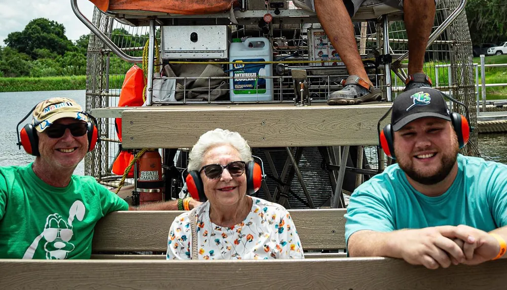 Three people wearing ear protection are smiling aboard what appears to be an airboat indicating a leisure activity likely involving a tour or exploration of a waterway
