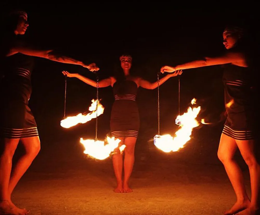 Three performers are swinging fiery poi in a coordinated fire dance at night