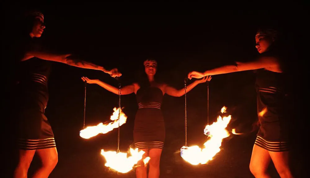 Three performers are swinging flames on chains in a coordinated fire dance at night