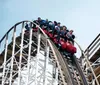 Thrilled riders are descending a steep drop on a wooden roller coaster against a clear sky