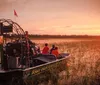 An airboat glides through a waterway at sunset carrying passengers who are likely enjoying a scenic tour