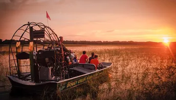 An airboat glides through a waterway at sunset, carrying passengers who are likely enjoying a scenic tour.