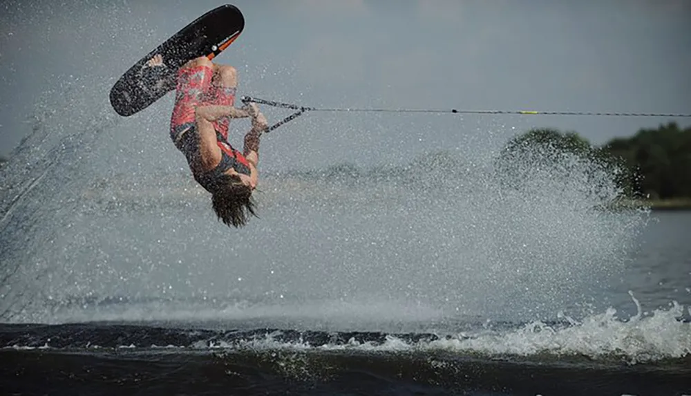 A person is captured mid-air while performing a flip during a wakeboarding trick creating a dynamic spray of water around them