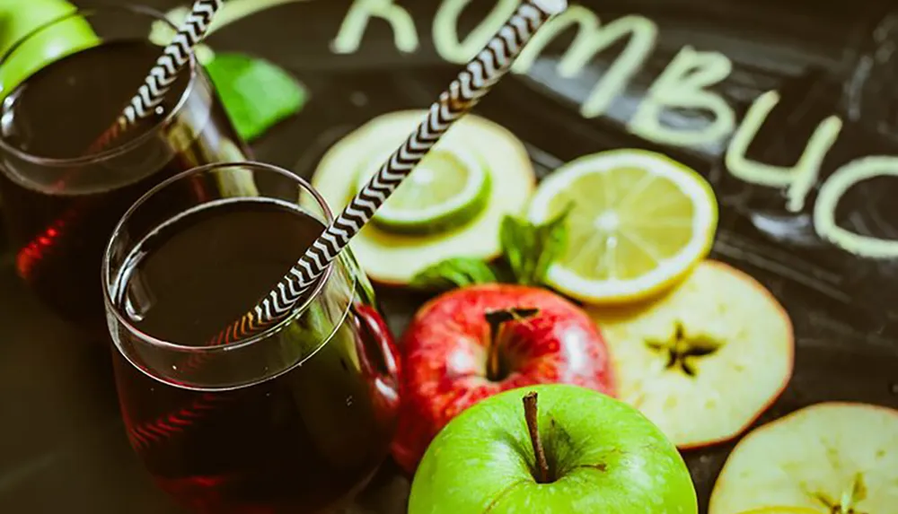 This image features a refreshing beverage setup with two glasses of a dark red drink complete with striped straws alongside fresh apples lime and lemon slices on a surface with RUMBL written in chalk suggestive of a relaxed casual drinking atmosphere