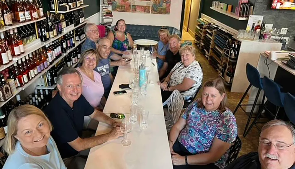 A group of people is smiling and posing for a photo at a long table in a cozy wine shop or bar