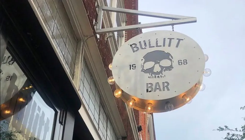 The image shows a circular outdoor sign for Bullitt Bar featuring a skull graphic and adorned with circular light bulbs around its perimeter against an urban building backdrop