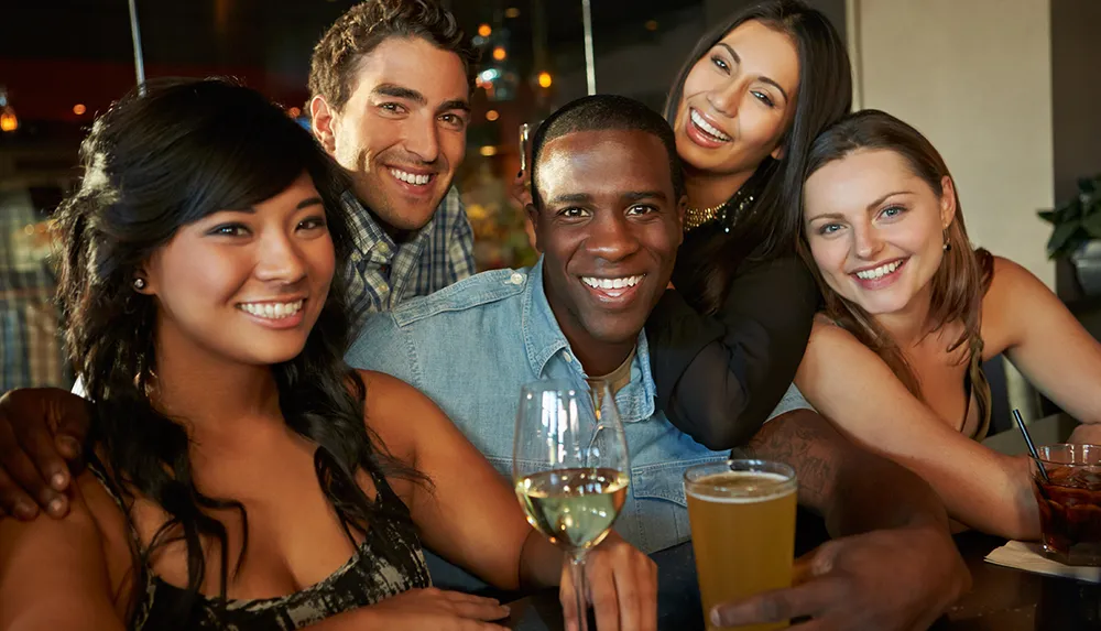 A group of five smiling friends enjoying drinks together at a social gathering