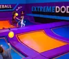 People of different ages are playing dodgeball on an indoor trampoline court with vibrant purple and blue colors