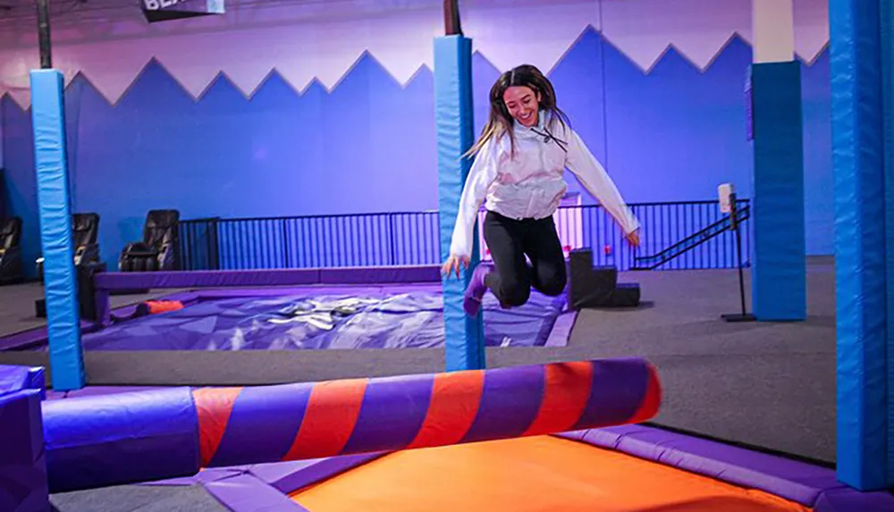 A person is joyfully jumping on a colorful indoor trampoline at a play center