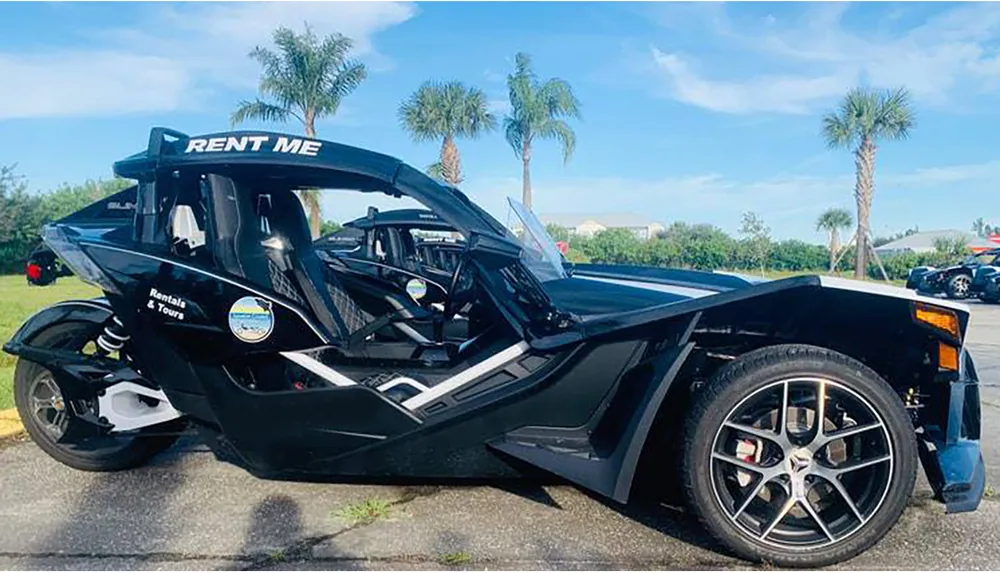 A black futuristic-looking three-wheeled vehicle with an open cockpit and a RENT ME sign is parked outdoors